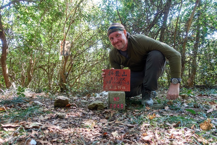男子站在新置山山頂三角點石碑後拿著標誌